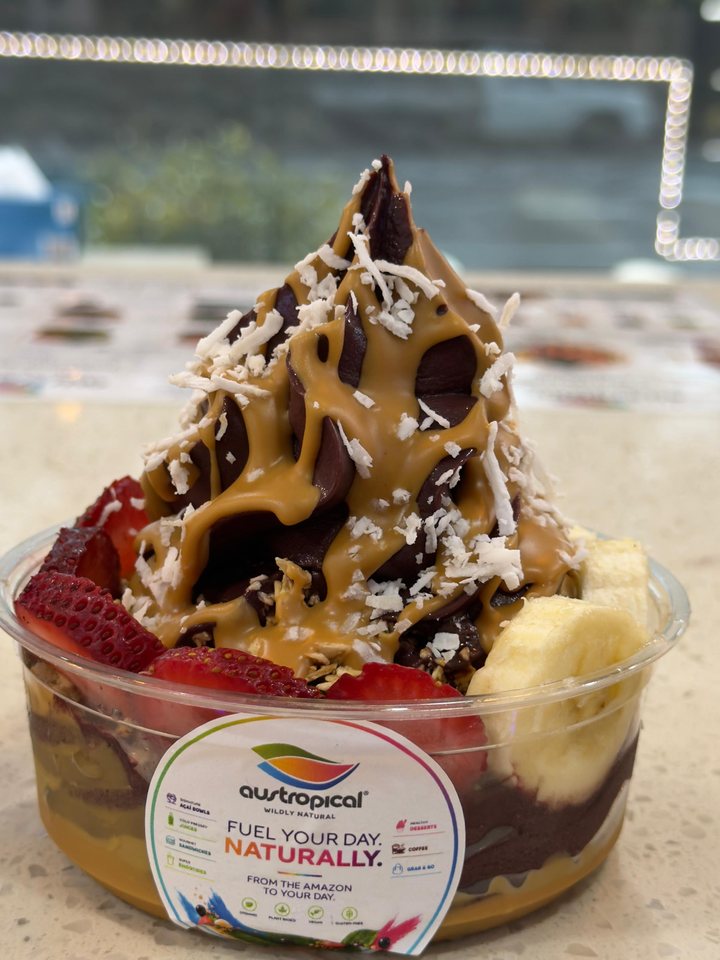 A tall açaí swirl under caramel sauce and shredded coconut, with strawberries and banana.