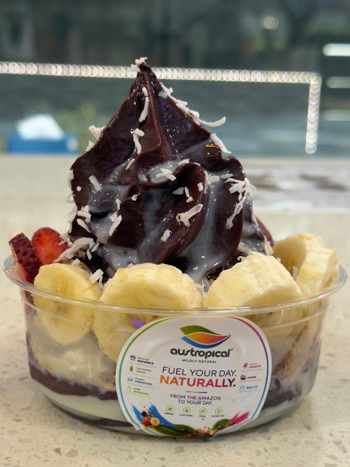 A swirl of açaí with a white drizzle and coconut over banana, on the café counter.