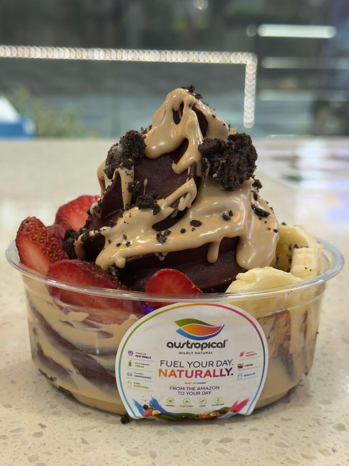 An açaí bowl with a creamy sauce and cookie crumbs over strawberries and banana, on the café counter.
