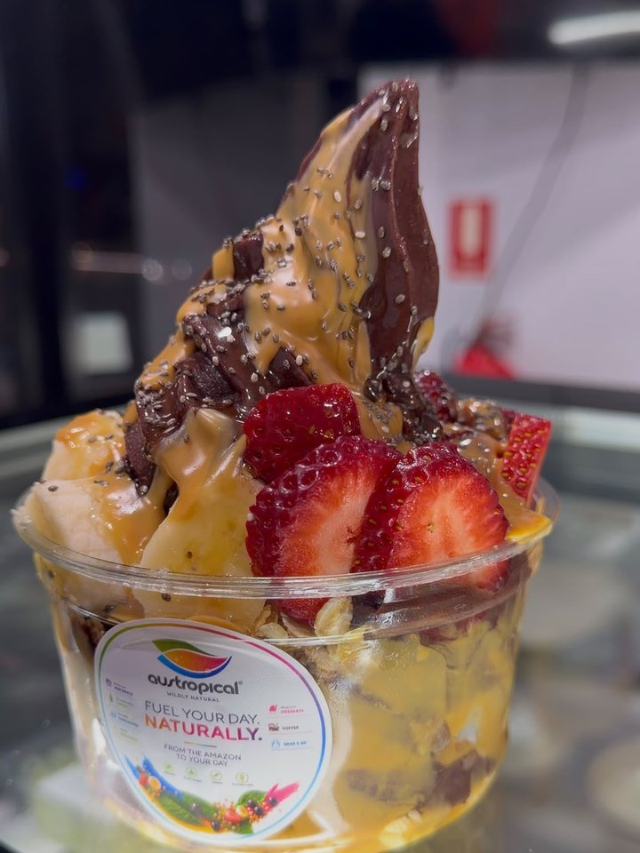 An açaí bowl with caramel and peanut sauces, banana and strawberries, on the glass dessert cabinet.