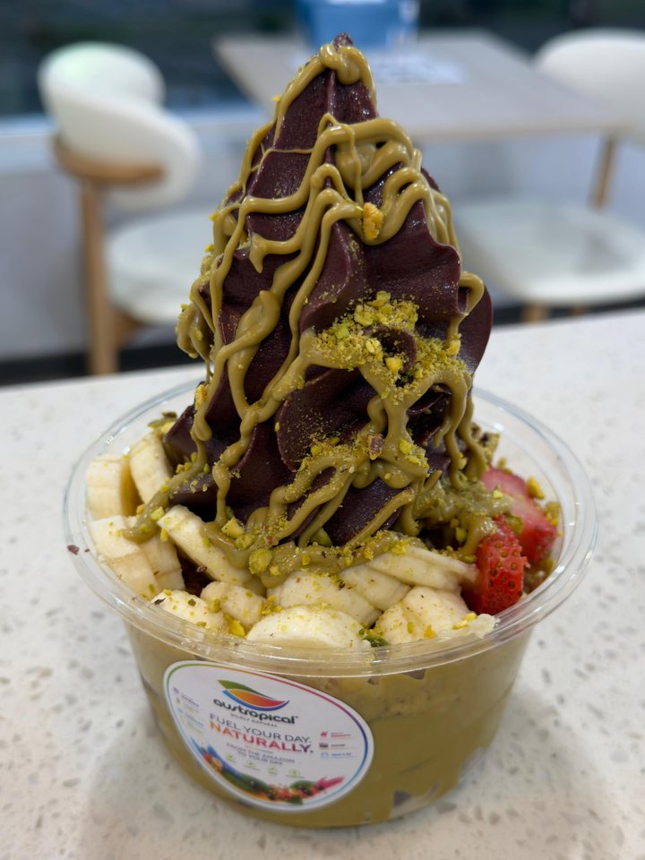 A tall açaí swirl under pistachio sauce over banana slices, on the café counter.