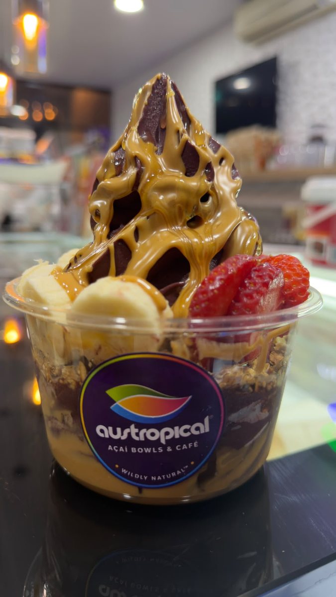 Açaí soft serve with a caramel-colored sauce, banana and strawberries in a clear Austropical cup on the café counter in Sydney.