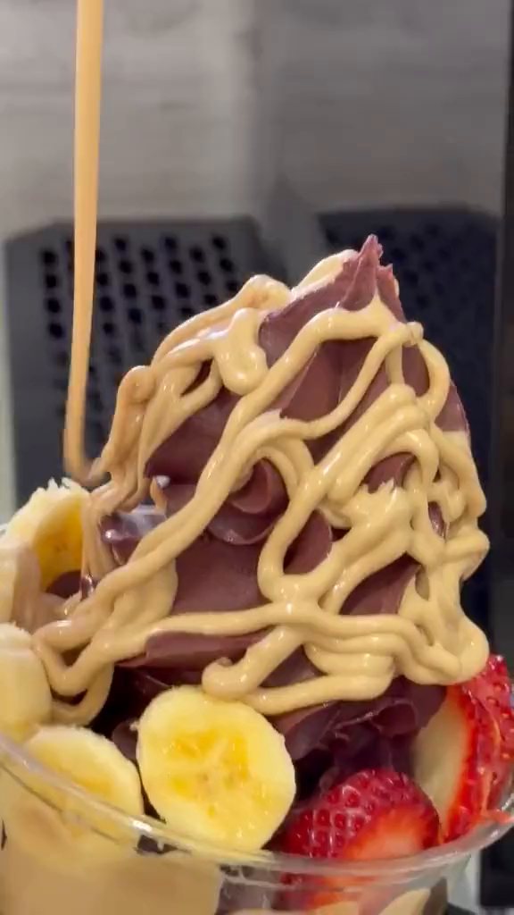 A light caramel-colored sauce drizzled over an açaí bowl with banana and strawberries, held in a gloved hand at the Austropical café in Sydney.