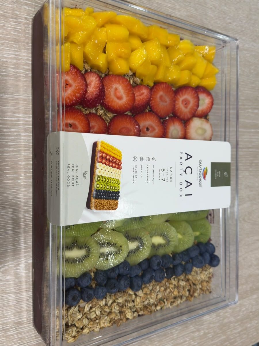 The café's large Açaí Party Box from above: rows of mango, strawberry, kiwi, blueberry and granola in a clear box, with its sleeve.