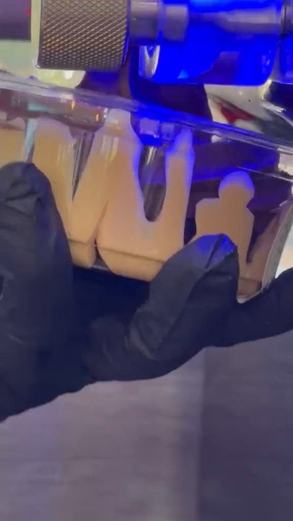Açaí soft serve pouring from the machine into a clear cup held in a gloved hand.