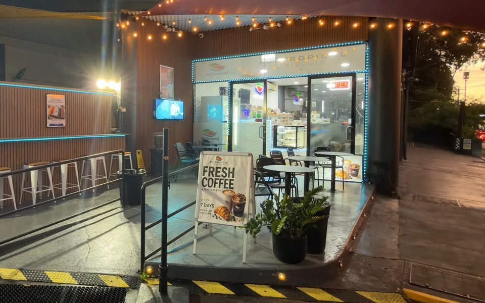 The Austropical café in Sydney at dusk: string lights over the patio, the lit shopfront and a sandwich board for coffee.