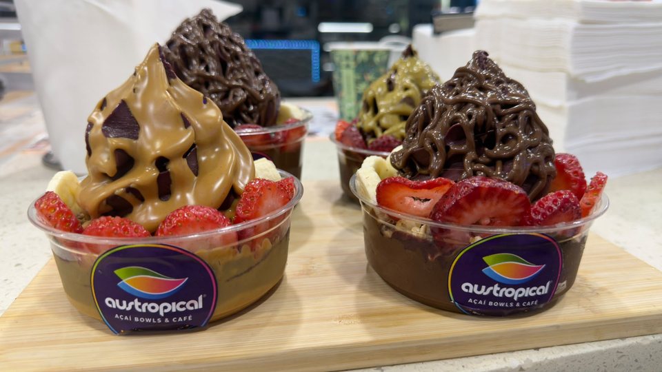 Three açaí cups with chocolate, caramel and pistachio tops on a wooden board.