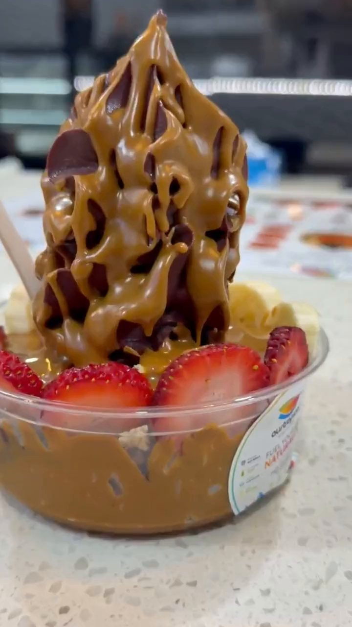 The camera circles a tall açaí soft-serve bowl with caramel sauce, strawberries and banana, then cuts to a second bowl.