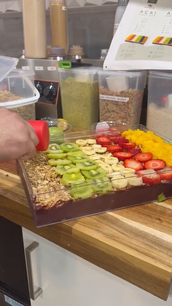 Gloved hands arrange rows of kiwi beside banana, strawberry and mango over the café Party Box.