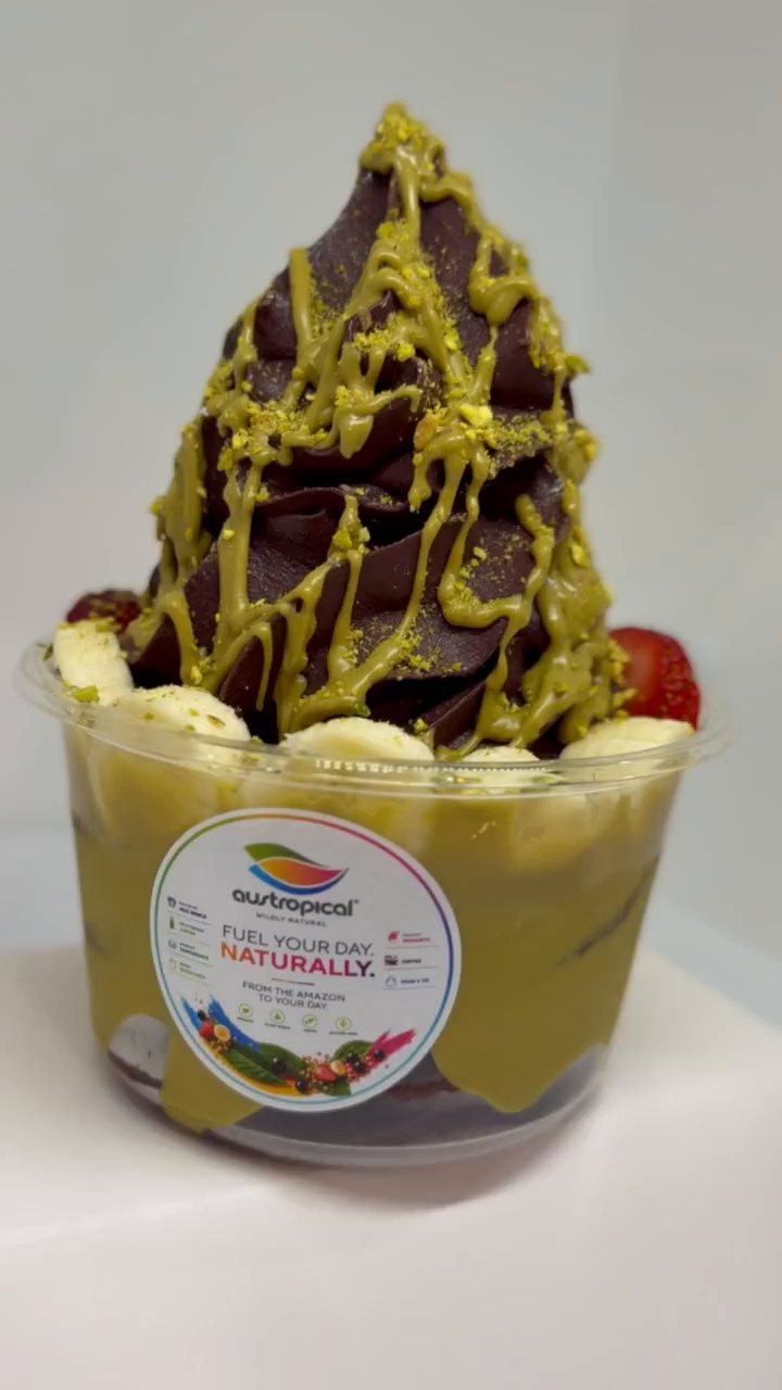 An açaí soft-serve bowl with pistachio sauce, crushed pistachio, banana and strawberry, turning slowly on a white table.