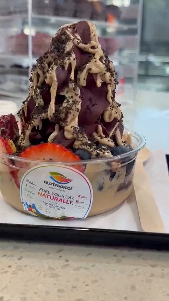Açaí soft-serve bowls with sauce, cookie crumbs, banana and strawberry on a tray, with spoons, at the counter.