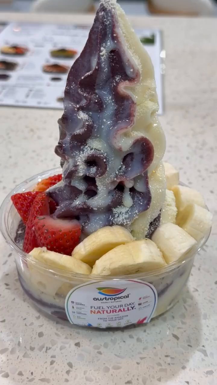 A tall açaí and vanilla soft-serve swirl with strawberry and banana, on the café counter.