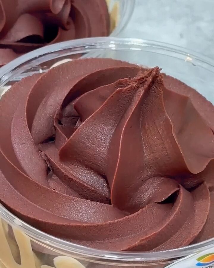 Close-up of a plain açaí soft-serve rosette in a clear tub, the camera easing in on its piped ridges.