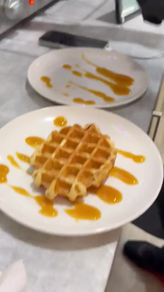 Gloved hands plate freshly made waffles behind the café counter.